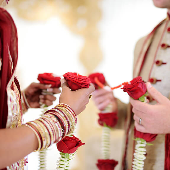 close-up of hands of indian bride and groom exchanging red roses garlands