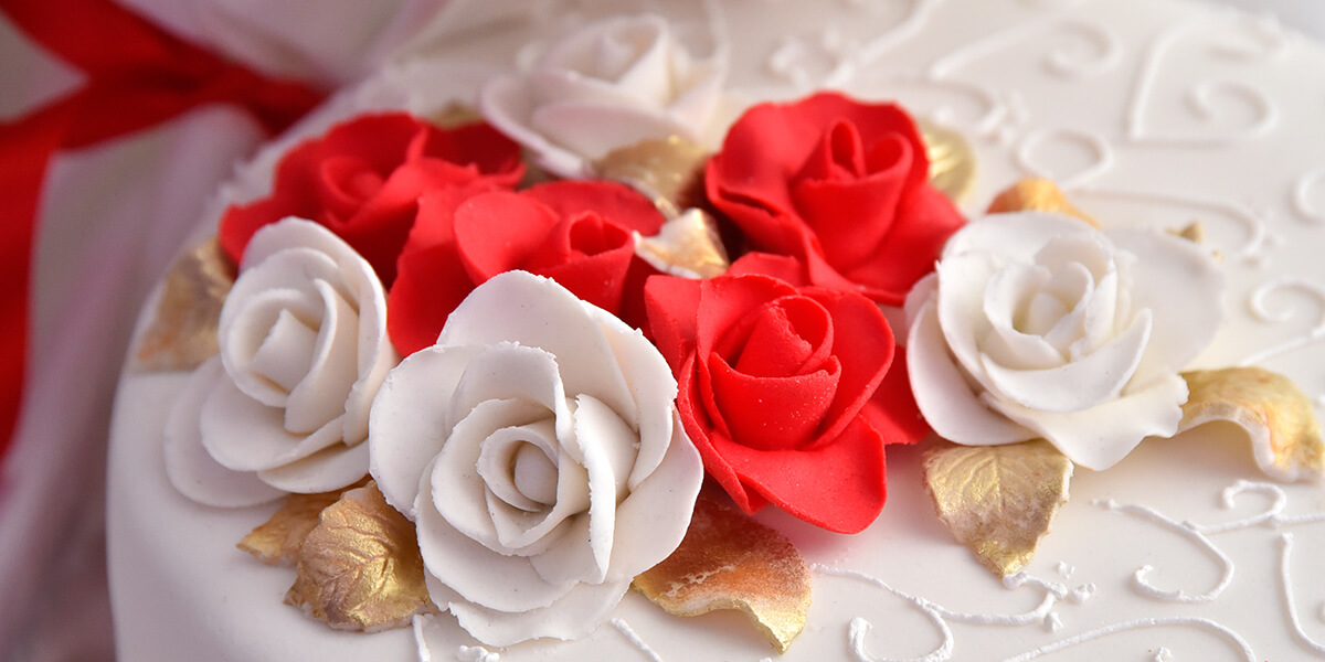 close-up of edible white and red roses on top of a white wedding cake
