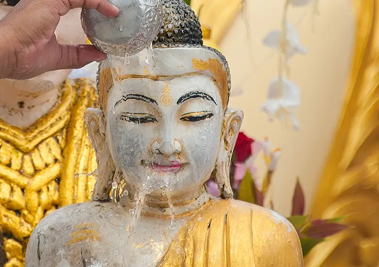 close-up of a serene white and gold Buddha statue with water gently flowing over the face during a traditional cultural ritual
