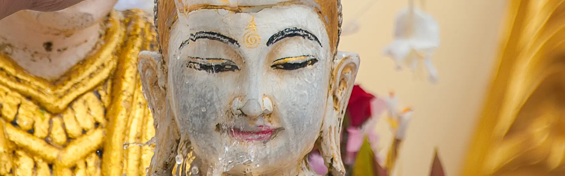 close-up of a serene white and gold Buddha statue with water gently flowing over the face during a traditional cultural ritual