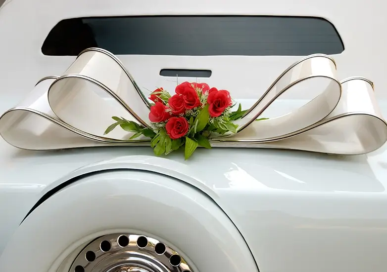 Elegant modern Indian wedding car decoration featuring silver-trimmed ivory ribbon loops and red rose bouquet by Cultural Event Rentals in Southern California