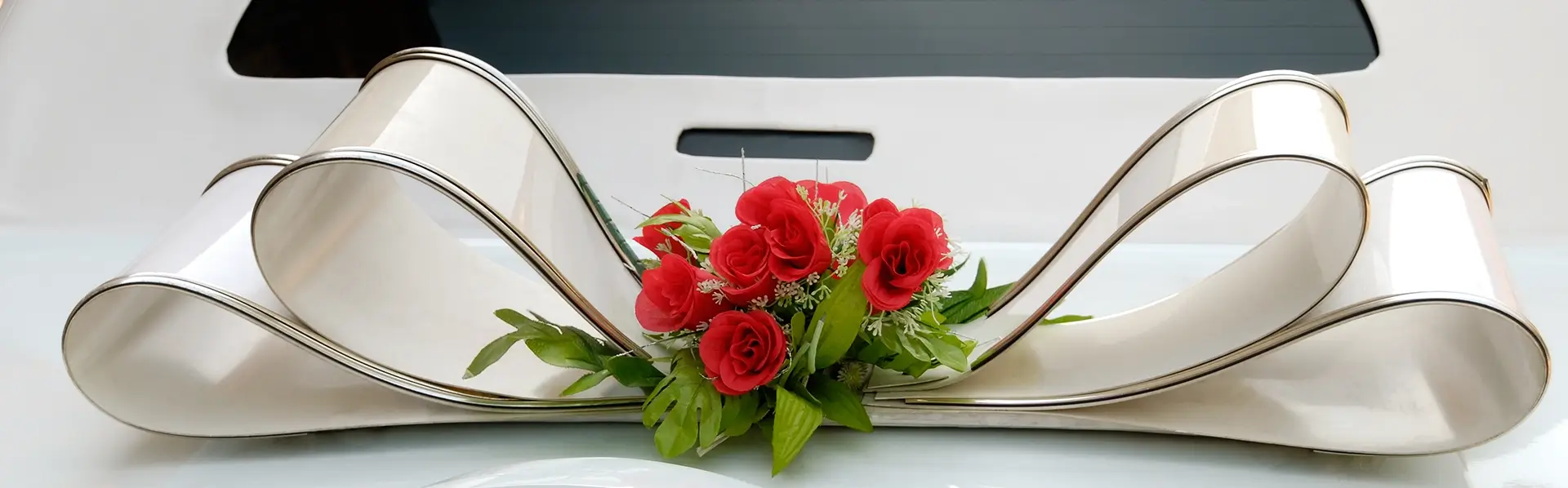 Elegant modern Indian wedding car decoration featuring silver-trimmed ivory ribbon loops and red rose bouquet by Cultural Event Rentals in Southern California