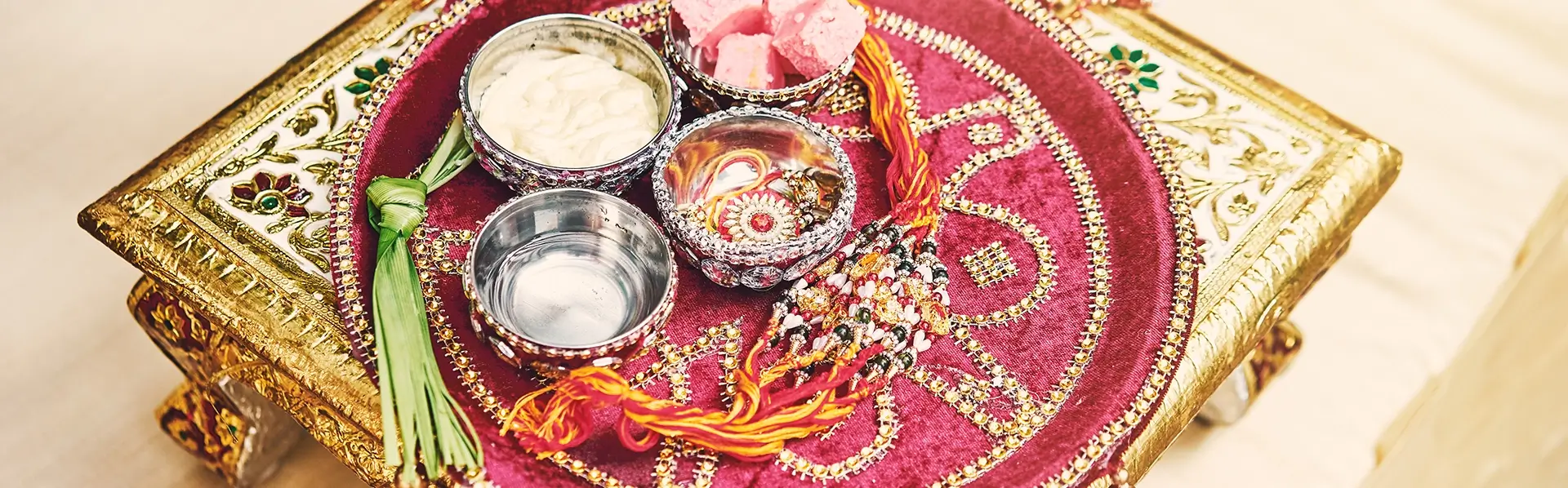 Vintage Indian wedding décor with ornate gold table, embroidered red velvet tray, and traditional silver bowls for ceremonial rituals.